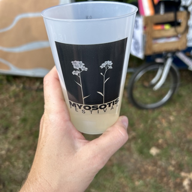 Eine Hand hält einen MYOSOTIS-Festivalbecher mit Vergissmeinnicht-Motiv