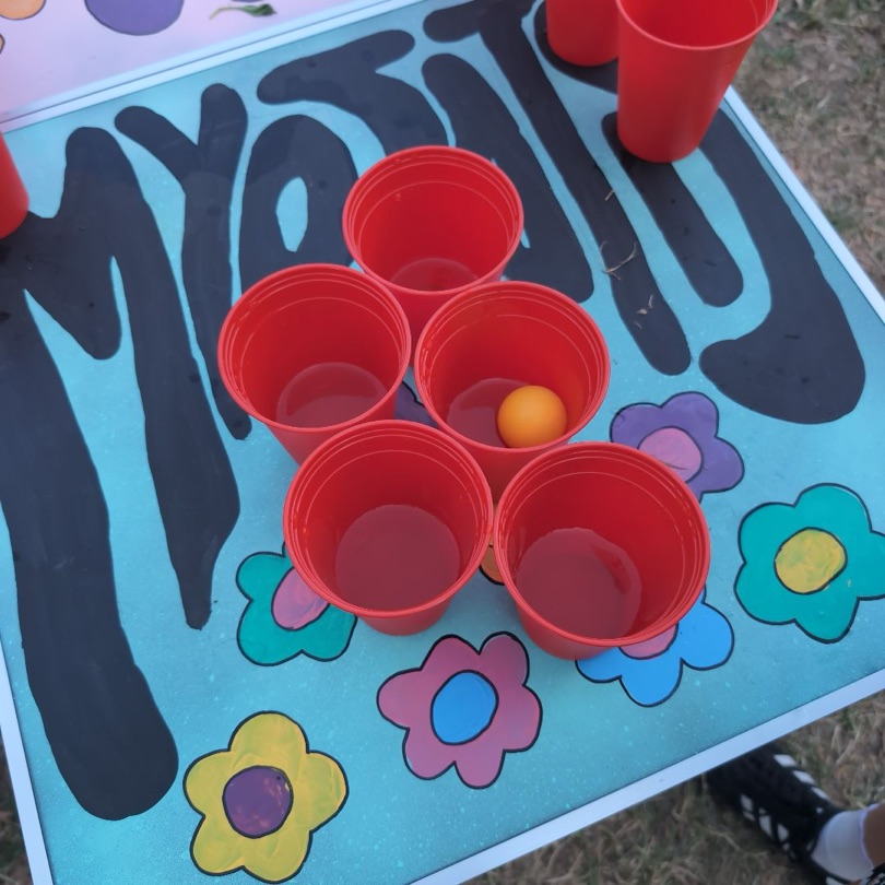 Rote Becher auf dem bemalten MYOSOTIS-Bierpong-Tisch mit Blumen und Schriftzug